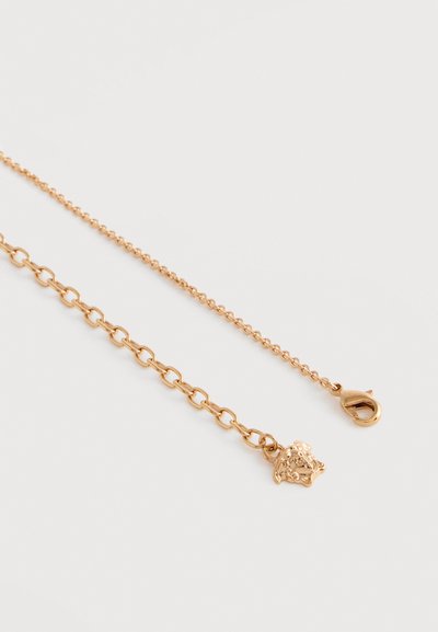 Κολιέ με αλυσίδα από χρυσό, με μικρό μενταγιόν κεφάλι λέοντα και κούμπωμα καβουριού σε απλό λευκό φόντο.