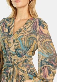 Sukienka o fasonie kopertowym z wirującym marmurkowym wzorem w odcieniach niebieskiego, złotego i różowego. Długie rękawy i związana talia nadają jej struktury.