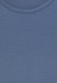 Gros plan sur un tissu en coton bleu montrant les coutures du col rond et la texture.