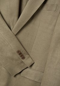 Brauner Leinenblazer mit Reverskragen, einer Rückenschlitz und vier braunen Knopfakzenten an den Manschetten. Strukturiertest Gewebe mit einem subtilen Glanz.