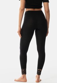 Leggings noirs avec une texture côtelée et un bord en dentelle au niveau des poignets, présentant une taille haute et une longueur au niveau des chevilles.