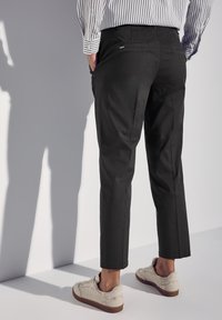 Svarta bomullsbukser med smal passform och kort längd, med bakfickor och flat midja, tillsammans med beige sneakers.