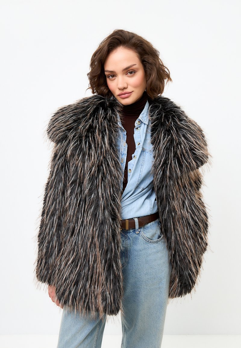 Palton din blană sintetică cu un model de culoare neagră și maro, având o textură pufoasă, guler lat și o croială lejeră, purtat peste o cămașă din denim.
