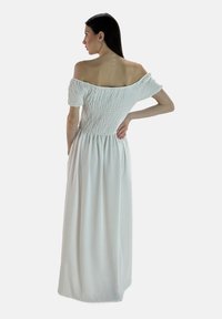 Hvid maxikjole med off-the-shoulder design, smocket bærestykke, korte puffærmer og svajende nederdel. Lavet af let, tekstureret stof.