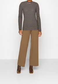 Stribet langærmet top i sort og beige, parret med brede brune bukser. Modellen har brune hæle støvler på, hvilket viser et afslappet outfit.