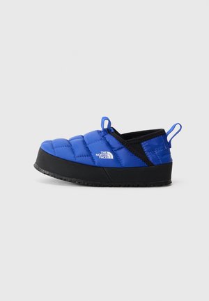 Chausson bleu en peluche avec une semelle en caoutchouc noir, présentant une tige texturée, une ouverture élastique et une languette pour un enfilage facile.
