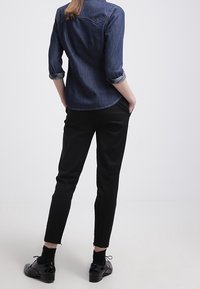 Mörk denimskjorta med uppvikt ärm, i kombination med svarta avsmalnande byxor och svarta snörskor. Skjortan har en spetsig krage och bakstycke.