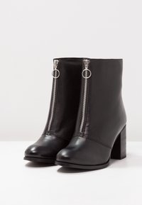 Černé kožené kotníkové boty se stříbrnými zipy, kulatou špičkou a robustním blokovým podpatkem. Hladká textura a minimalistický design.