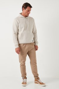 Hoodie beige chiaro con tasca frontale, cappuccio con stringhe e polsini a costine, abbinato a pantaloni jogger color sabbia e sneakers alte marroni.