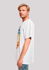 White cotton t-shirt featuring a circular, multicolored graphic design with blue, green, yellow, and orange stripes. Short sleeves, relaxed fit.
