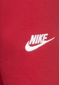 Röd bomullstyg med en framträdande vit broderad Nike-logotyp. Materialet har en slät textur utan ytterligare mönster eller accenter.