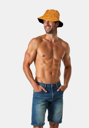 Sombrero de cubo naranja con detalles negros y un patrón divertido, llevado por un hombre en pantalones cortos de mezclilla, que muestra una figura muscular.