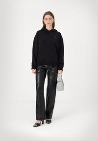 Felpa nera oversize con polsini a costine, abbinata a pantaloni in pelle nera a vita alta e décolleté nere a punta. Inclusa borsa a tracolla blu chiaro.