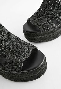 Schwarze Plattform-Sandalen aus gewebtem synthetischem Material mit floralen Mustern, einer glatten Lederfußbett und einer strukturierten, geflochtenen Sohle.