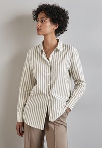 Camicia a righe bianca e beige con colletto, maniche lunghe e orlo arrotondato, abbinata a pantaloni beige. Tessuto di finitura liscia.