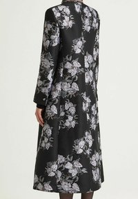 Vestito nero a fiori in tessuto satinato, con maniche lunghe e design a tutta lunghezza decorato con motivi floreali bianchi e argento.