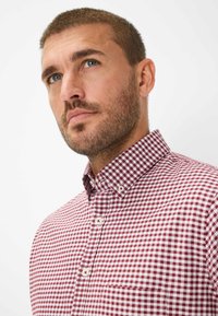 Rot-weiß kariertes Hemd mit Knöpfen und Kragen. Verfügt über eine Tasche auf der linken Seite und hat eine glatte, baumwollartige Textur.