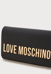 Melnā mākslīgā āda maciņš ar zelta toņu "LOVE MOSCHINO" uzrakstu. Taisnstūra forma, gluda virsma un redzamas šuvju akcenti.