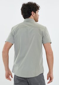 Camisa de mangas cortas en gris claro, con un cuello tipo polo y una textura suave. La vista trasera destaca un dobladillo curvo y costuras mínimas.