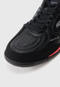 Black athletic shoe featuring leather and suede materials, textured surface, rounded toe, lace-up design, and red accents on the sole.