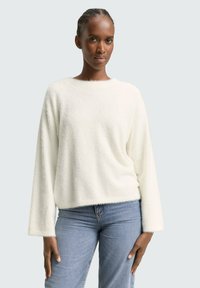 Weißer, flauschiger Pullover mit rundem Halsausschnitt, überschnittenen Schultern und langen Ärmeln, kombiniert mit hellblauen Jeans.
