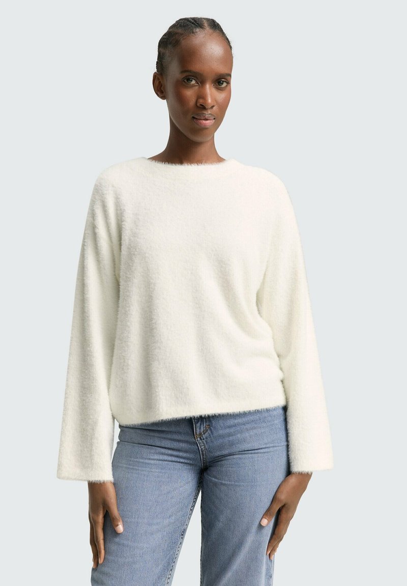 Weißer, flauschiger Pullover mit rundem Halsausschnitt, überschnittenen Schultern und langen Ärmeln, kombiniert mit hellblauen Jeans.