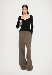 Sort langærmet bluse med sød hjerteudskæring, parret med brune vide bukser. Outfittet har bløde teksturer og diskrete draperinger.