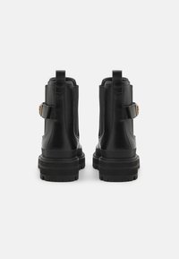 Botas de tobillo de cuero negro con una suela resistente, paneles laterales elásticos y una correa con una hebilla decorativa. Parte superior texturizada y talón reforzado.
