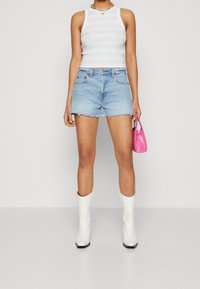 White striped tank top paired with light blue denim shorts featuring frayed edges. White cowboy boots and a small pink handbag.