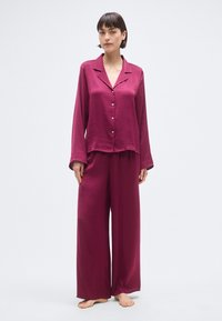 Ensemble de pyjama bordeaux deux pièces en tissu lisse. Chemise à manches longues avec col et boutons sur le devant, et pantalon à jambes larges, tous deux avec une coupe décontractée.