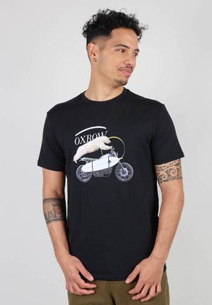 T-shirt en coton noir avec un design graphique représentant un animal blanc sur une moto, avec le texte "OXBOW" au-dessus. Manches courtes, col rond.