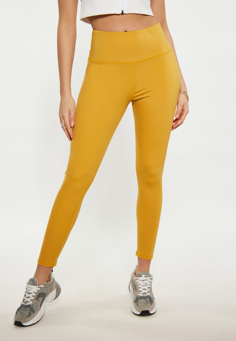 Magas derékú sárga leggings, rugalmas anyagból készült, testhez álló fazon, sima textúrával, karcsú sziluettel és látható minták nélkül.