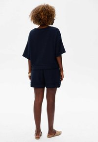 Granatowa, krótki rękaw, teksturowana bluzka połączona z dopasowanymi szortami. Luźny krój z widocznymi akcentami szwów. Noszona z beżowymi butami wsuwanymi.
