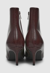 Stivaletti alla caviglia in pelle bordeaux con finitura lucida, alti tacchi a spillo, chiusure con zip e un design elegante e affilato.