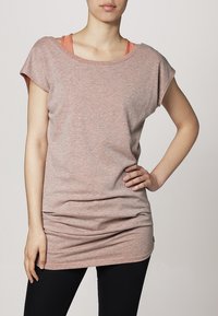 T-shirt rose clair à manches courtes en tissu doux, avec un large col et une coupe décontractée, superposé à un débardeur orange.
