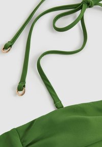 Zelený textilný top s úzkymi ramienkami. Ramienka majú na koncoch zlaté krúžky a látka má hladkú, matnú textúru.