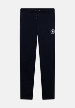 Pantalones de chándal azul marino con cinturilla elástica, cordón y un pequeño logo blanco en el muslo. Tejido suave y liso, con un corte ajustado en los tobillos.