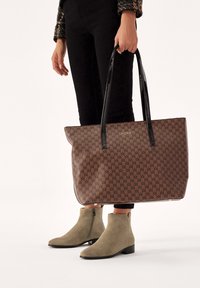 Geanta tote cu model brown, mânere negre lucioase, având un logo auriu. Purtați cu blugi negri și botine din suede verde.