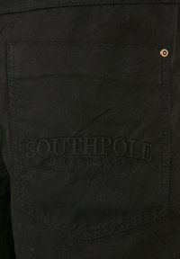 Sort stof med en tekstureret overflade. Har en baglomme præget med "SOUTHPOL" samt et lille metalnitterdetalje.