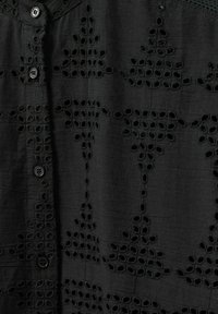 Black button-up shirt featuring embroidery with cut-out floral patterns, smooth texture, and round black buttons along the front.