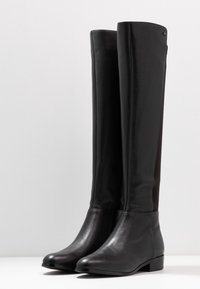 Botas de cuero negras hasta la rodilla con una textura suave, diseño ajustado y un tacón bajo en bloque; cuenta con cremallera lateral y panel de tela suave.