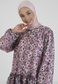 Long-sleeved dress in sheer fabric featuring a pink floral pattern on a gray background, with a gathered ruffle at the hem.