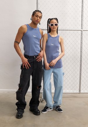Blå ribbede tank tops med hvite logoer, svarte ripped jeans og lyseblå brede bukser. Tilbehøret inkluderer hvite solbriller og svarte joggesko.