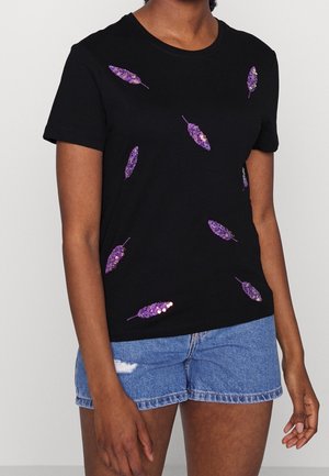 Czarny T-shirt z fioletowymi cekinowymi wzorami piór, krótkimi rękawami i okrągłym dekoltem. W połączeniu z jasnoniebieskimi jeansowymi szortami.