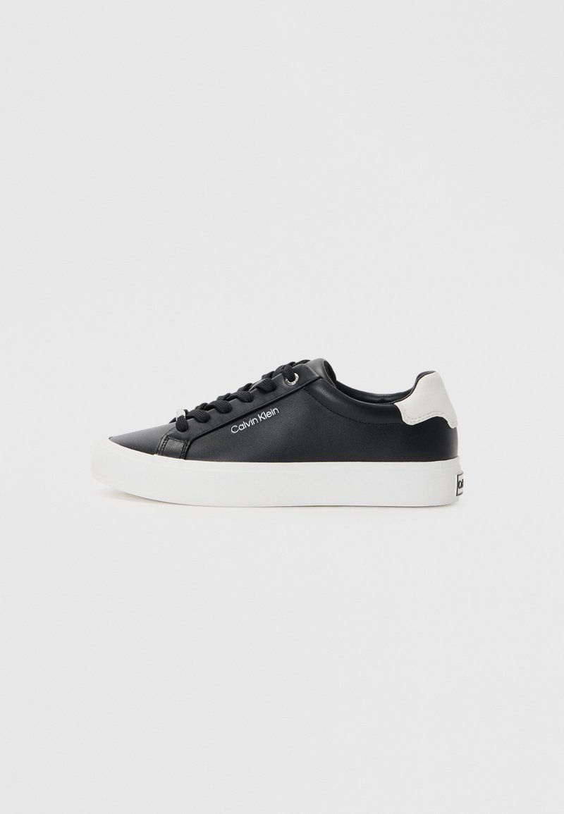 Fekete sneaker sima bőr felsőrésszel, fehér gumi talppal és kerek orral; fekete fűzőkkel és krémszínű kiemeléssel a saroknál.