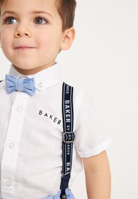 Biela košeľa s krátkym rukávom a logom "BAKER", modrá látková kravata, námornícke traky s bielym textom. Svetlomodré nohavice dokončujú outfit.