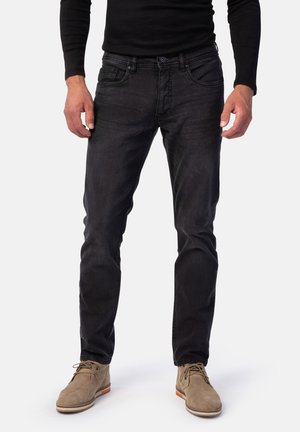 Black denim jeans with a slim fit, featuring front pockets, a zip fly, and light distressing. Paired with beige suede shoes.