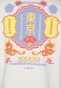 Röda och gula drakar flankerar ett märke med Tokyo-kanji, en röd fläkt och texten "NOODLE" och "TERRACE" på en vit bakgrund.