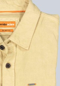 Helles beiges Hemd mit enganliegendem Schnitt, ausgestattet mit einem spitzen Kragen, dunklen Knöpfen und orangefarbenen Akzenten auf dem Etikett und der Naht.