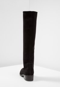 Botte noire en daim au-dessus du genou avec une texture lisse, un bout arrondi et un talon bas et épais. Présente une couture le long de l'arrière.